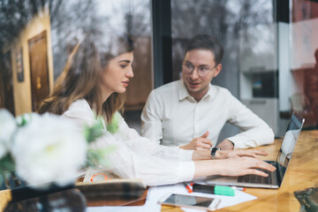 Man looking at female colleague typing on laptop