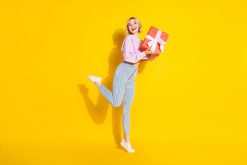 Full length profile side photo of young girl happy positive smile hold gift box celebration isolated over yellow color background