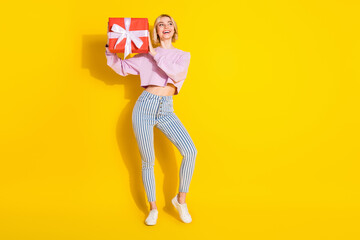 Full size photo of happy excited cheerful young girl look copyspace hold birthday present isolated on yellow color background