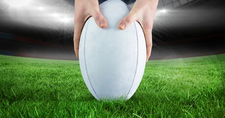 Close up of hands placing a rugby ball on grass field against stadium