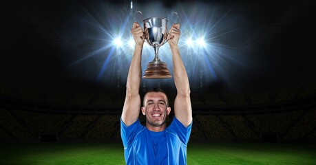 Portrait of caucasian male athlete lifting a trophy against floodlights in background - Powered by Adobe