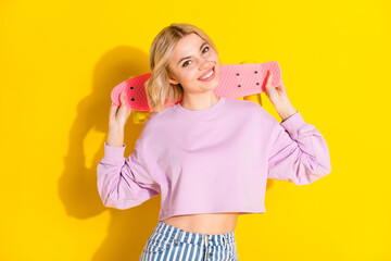 Photo of charming happy pretty young lady hold longboard behind head smile isolated on yellow color background