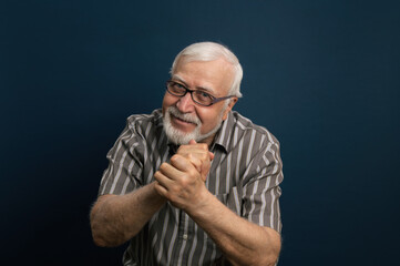 Handsome elderly energetic, charismatic gray-haired man in glasses, folded his hands, emotions in the frame, half-length portrait, blue background