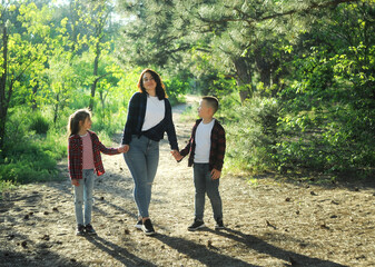 Obraz premium Young woman plays with children outdoors. Walking summer hike in the forest with children. 