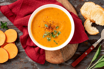 Creamy sweet potato soup with carrots and spices in a white bowl on a dark background top view. Tasty vegan sweet potato soup, autumn food.