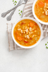 Soup with beans and vegetables in a bowl on a gray concrete background top view. Soup from lentils, chickpeas, beans, carrots, peppers, and tomatoes. Tasty vegan soup, vegetarian food. Copy space