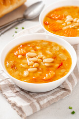 Soup with beans and vegetables in a white bowl on a gray concrete background closeup. Soup made from lentils, chickpeas, white beans, carrots, peppers, and tomatoes. Tasty vegan soup, vegetarian food.