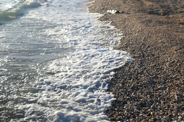 Pebbles and water on a beach, illuminated by golden hour light. Selective focus.