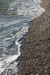 Pebbles and water on a beach, illuminated by golden hour light. Selective focus.