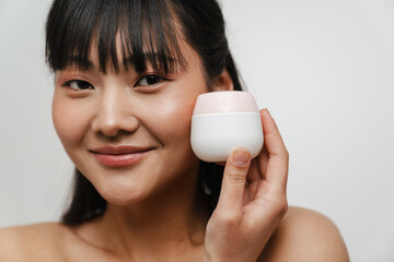 Young asian shirtless woman smiling while posing with face cream