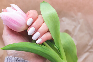 Female hand with beautiful manicure - white ivory nails with tulip on kraft paper blurred background, closeup. Selective focus