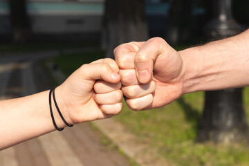 Father and child daughter bumping fists against blurred nature outdoor background. Trust, care and...