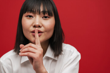 Fototapeta premium Young asian brunette woman showing silence gesture at camera