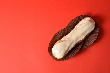 Directly above of Classic French dessert. Eclair with white chocolate on top filled with custard cream served on dessert paper pieces. Puffy Eclair on red background. Choux pastry. Copy space image
