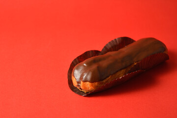 Close-up to classic French chocolate dessert eclair filled with custard isolated on red background....