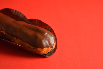 Close up to part of French dessert on red background. Eclair with custard filling and dark chocolate on top. Copy space image creative concept. Sweet menu object
