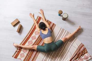 A woman in sportswear, doing yoga, performs a samokanasana exercise while sitting on a blanket, a...