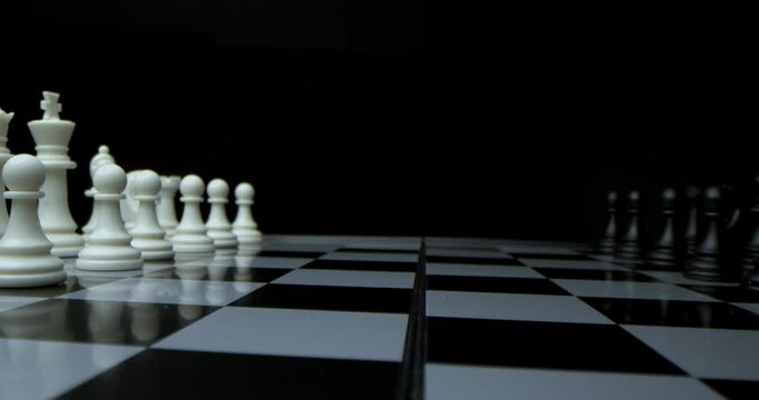 Game of chess. Filmed in a dark key. Super-macro photography of a chessboard with chess, camera travel on a slider from white pieces to black ones.