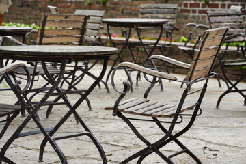 Fototapeta na wymiar On a terrace there are empty tables and chairs made of wood and metal, in front of a brick wall