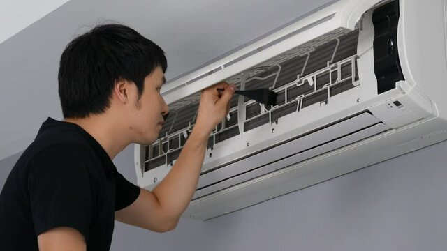 Young man using brush to cleaning the air conditioner indoors at home