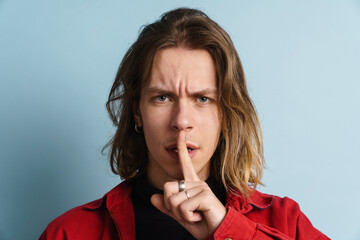 Young white man frowning while showing silence gesture at camera