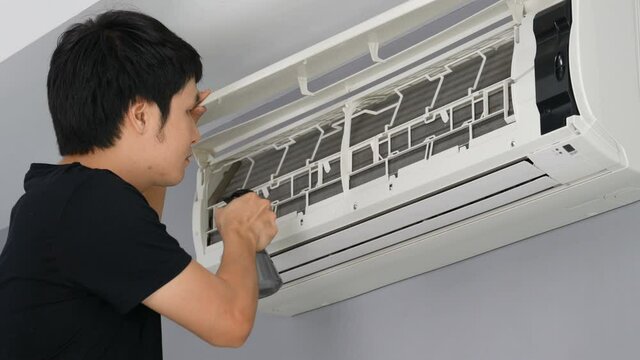 Young man cleaning the air conditioner indoors at home