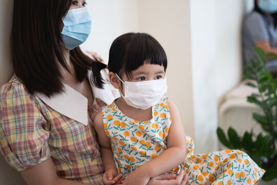 Mother And Daughter Wearing Surgical Mask Sitting On The Table In The Hospital