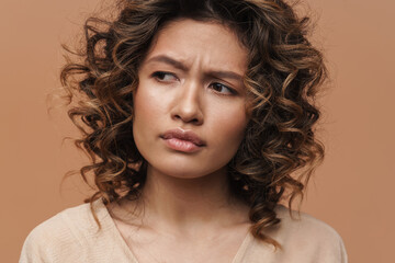 Young curly hispanic woman frowning and looking aside