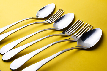 Close-up and selective focus of the set of dinning cutlery on a yellow background. Flat lay and top view of a spoon, fork, and knife with copy space. Kitchen equipment for food.