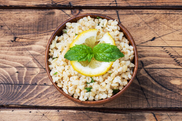 Boiled bulgur with fresh lemon and mint on a plate. A traditional oriental dish called Tabouleh. wooden background rustic top view, copy space