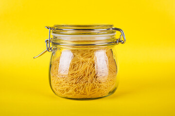 pasta in a glass jar on a yellow background isolated