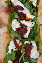 Gourmet pizza texture and pattern. Overhead closeup view of fresh arugula, Italian burrata cheese and sun dried tomatoes pizza. 