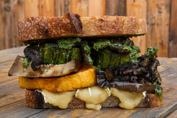Gourmet food. Closeup view of healthy grilled vegetables sandwich, with eggplant, brie cheese, squash, mushrooms, zucchini and arugula pesto, on the rustic wooden table with a wooden background.