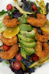 Mediterranean salad. Overhead closeup view of colorful salad with lettuce, cabbage, tomatoes, fried shrimps, avocado and orange, served on a white dish.