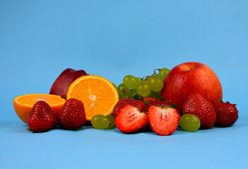 Pile of various fresh fruits on a blue background stock images. Group of fruits isolated on a blue background with copy space for text. Strawberries, oranges, apples, grapes stock photo