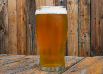 Craft beer. Closeup view of a golden honey beer with perfect foam in a glass on the wooden table with a wooden background.
