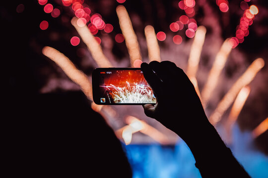 Crop spectator recording video of firework on smartphone