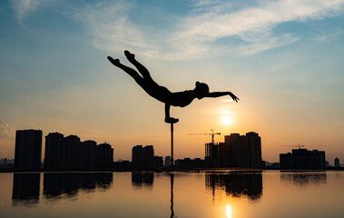 Flexible acrobat doing handstand on the cityscape background during dramatic sunset. Concept of...