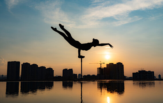 Flexible acrobat doing handstand on the cityscape background during dramatic sunset. Concept of willpower, control and dream