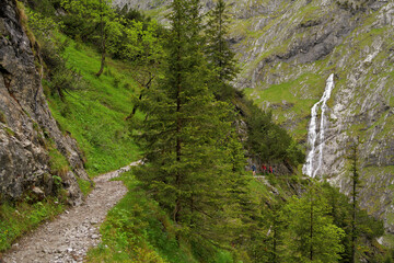 Fototapeta na wymiar Wanderer auf einem Wanderweg im Höllental mit einem Wasserfall 