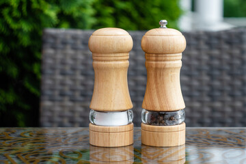 Salt and black pepper shakers in a summer cafe, a wooden pepper mill on a table in a restaurant....