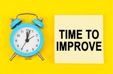 On a yellow background lie a clock and a sticker sheet with the inscription - TIME TO IMPROVE