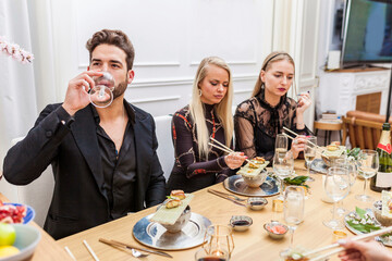 Group of friends eating sushi and drinking wine at home dinner