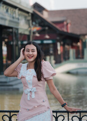 portrait of cheerful Asian woman tourist happy laughing looking away standing on bridge near river in town