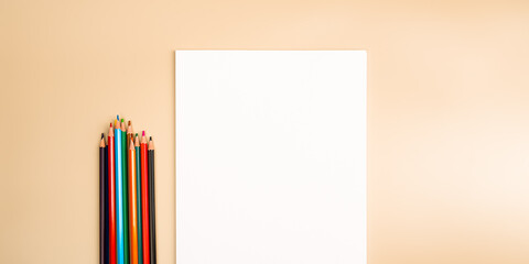 A blank white sheet and colored pencils for drawing on a plain textured background with space for...