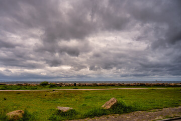 Fototapeta premium A beautiful, dramatic sky over the ocean. A lawn and stones in a wave breaker in the foreground. Picture from Malmo, Sweden