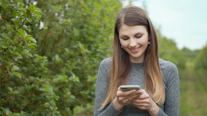 Happy young woman use smartphone standing in park sun outdoor health hand girl tree sport fitness summer nature internet technology female runner exercise phone workout mobile cell phone