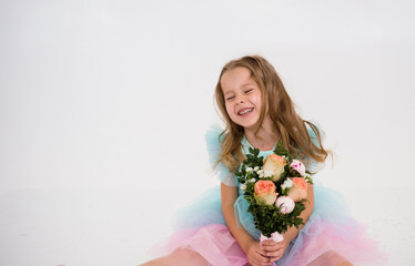 a happy little girl in a festive dress sits and holds a bouquet of flowers on a white background with a copy of the space