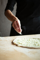 Hands of chef are preparing pizza. Pours cheese onto rolled dough