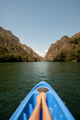 Kayaking through river in Matka canyon, Macedonia. Woman legs in the blue kayak - obrazy, fototapety, plakaty